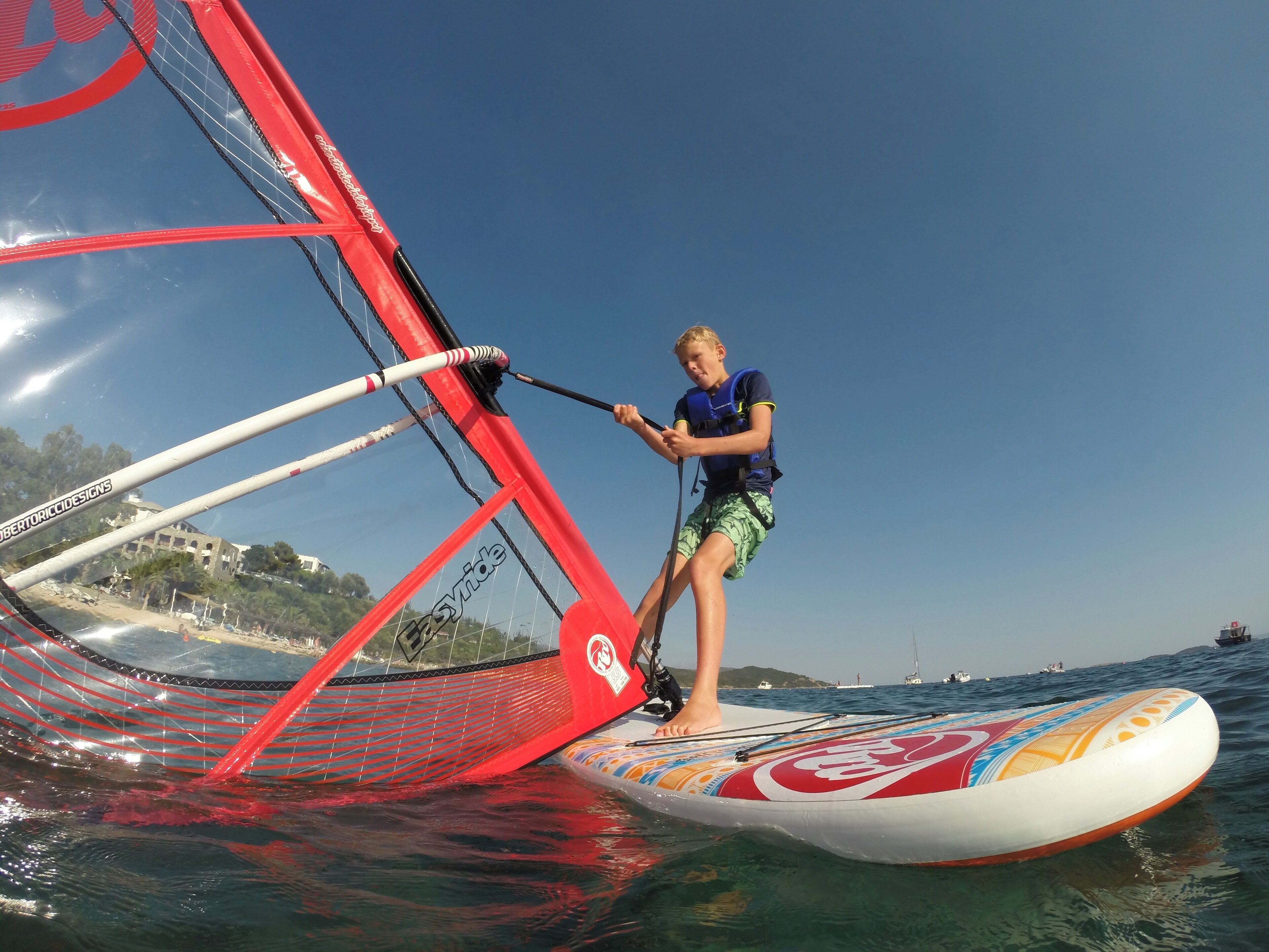 A person windsurfing on a board with a red sail.