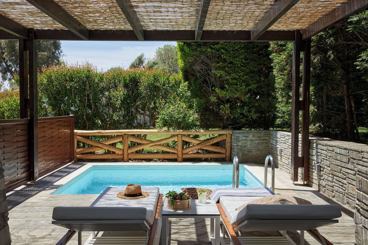 A covered outdoor swimming pool with lounge chairs and a wooden fence.