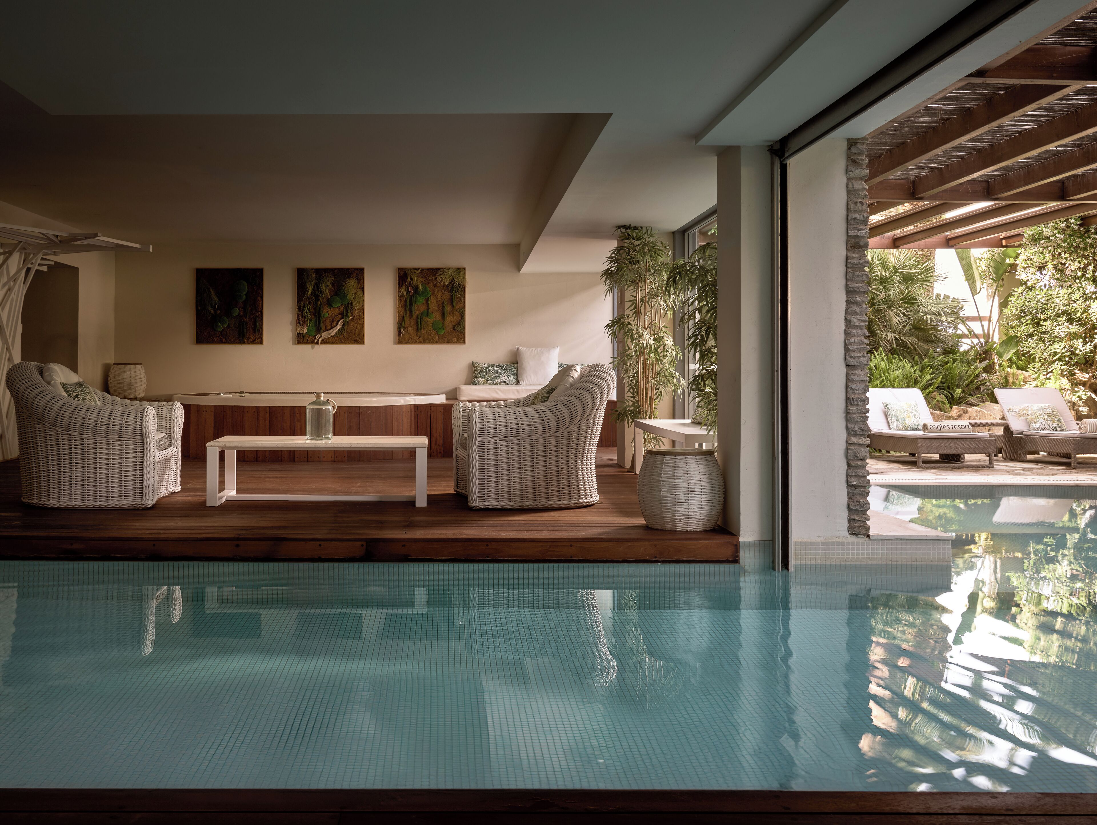 Zona junto a la piscina con mobiliario de mimbre, una mesa y vistas a la piscina.