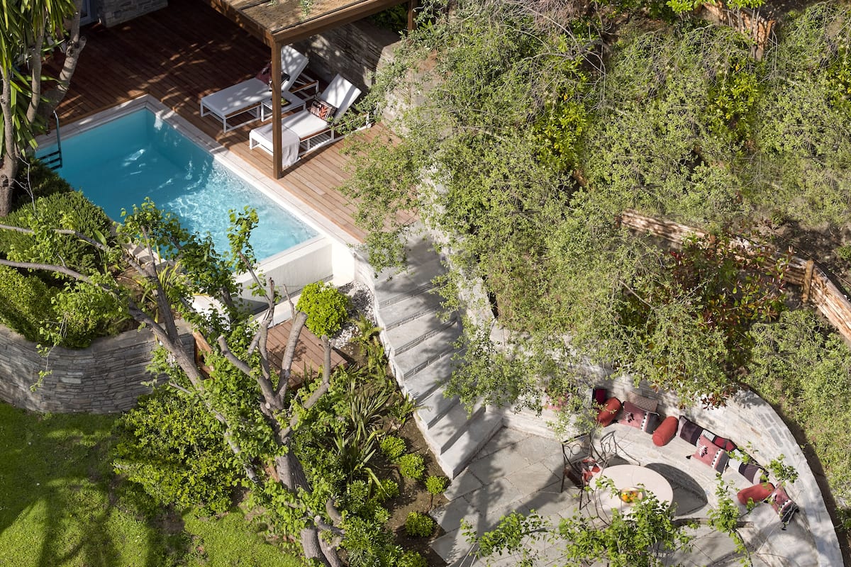 A pool area with a wooden deck, lounge chairs, and a stone wall.