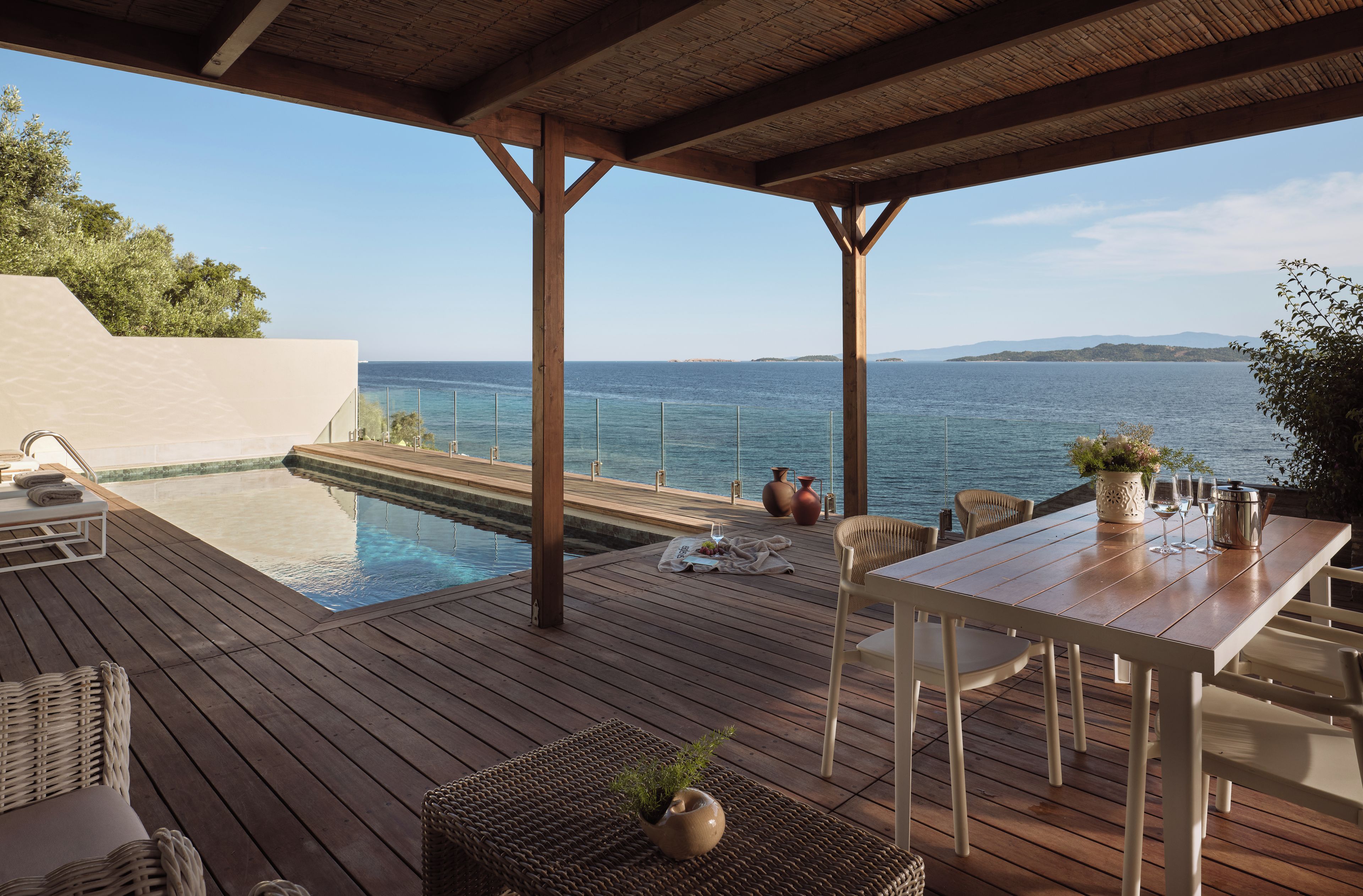 Una terraza de madera con piscina, mobiliario exterior y vista al mar.