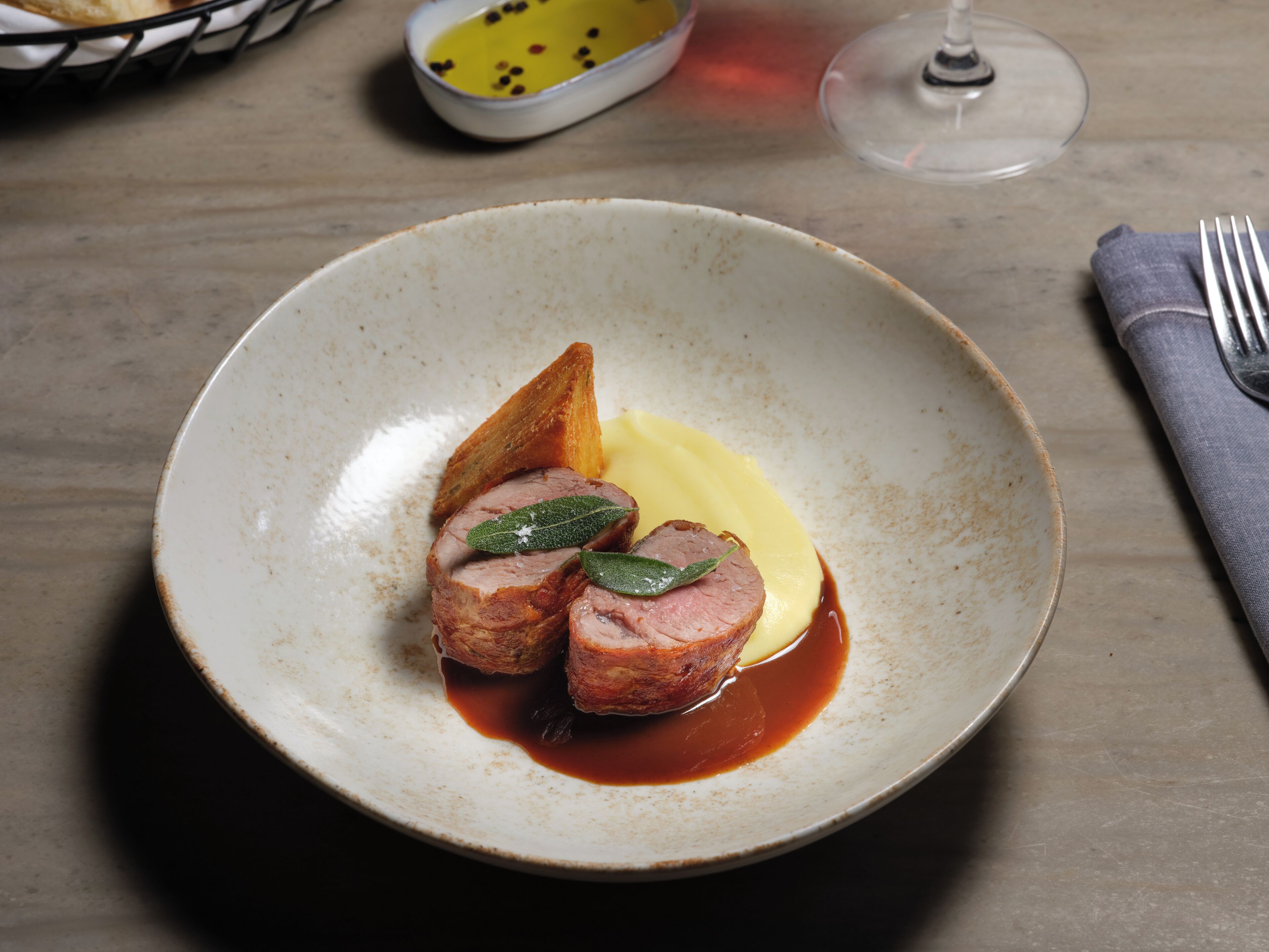 A plate with sliced meat, a garnish, and a sauce on a ceramic dish.