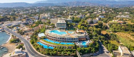 A resort with a central swimming pool, multiple buildings, and a coastal view.