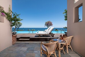 A poolside area with a lounge chair, a table with a bottle, and a view of the sea.