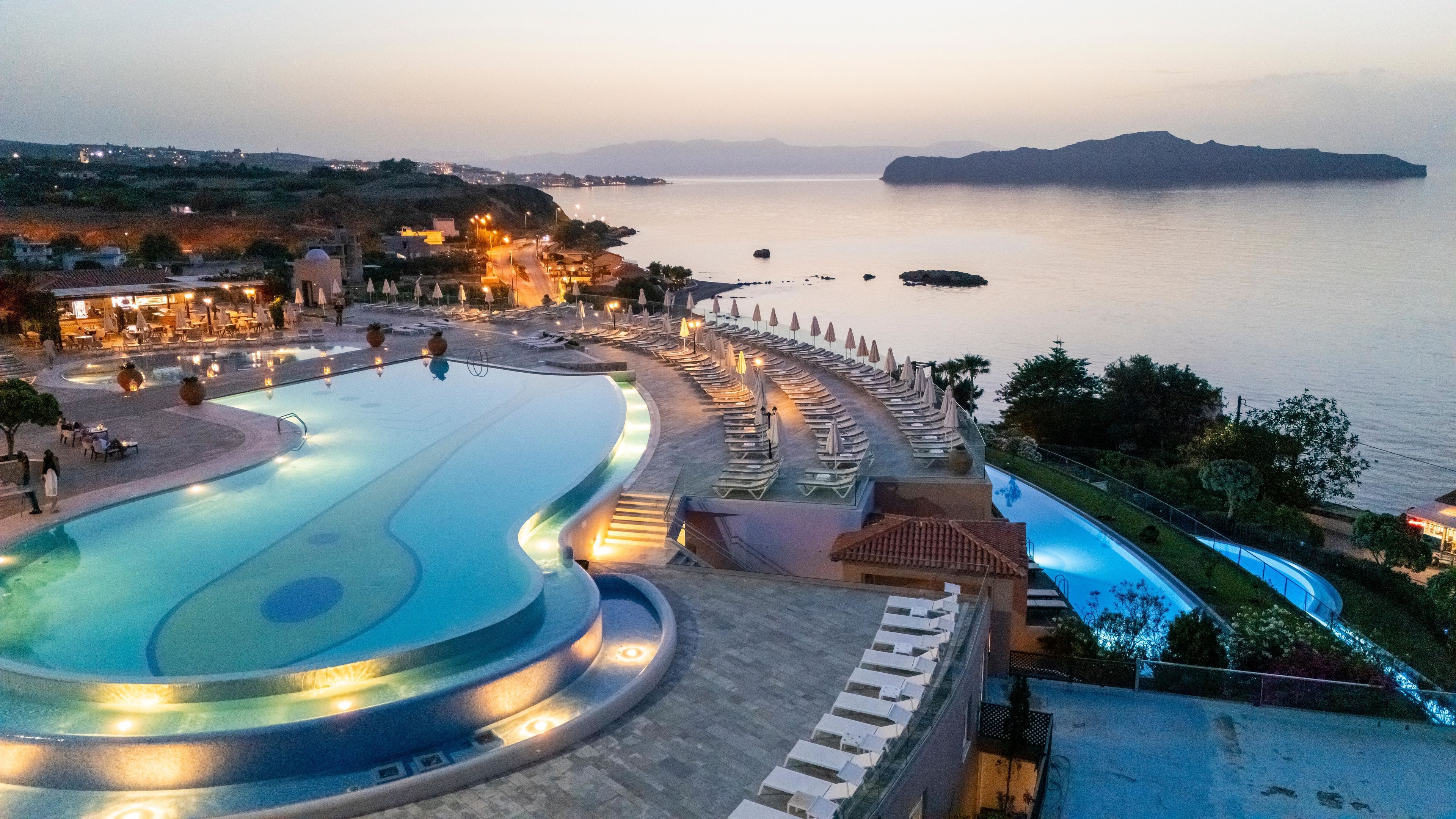 Un resort con una amplia piscina, tumbonas y vista al mar.