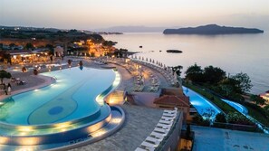 A resort with a large infinity pool, a beach area with sun loungers, and a view of the sea.