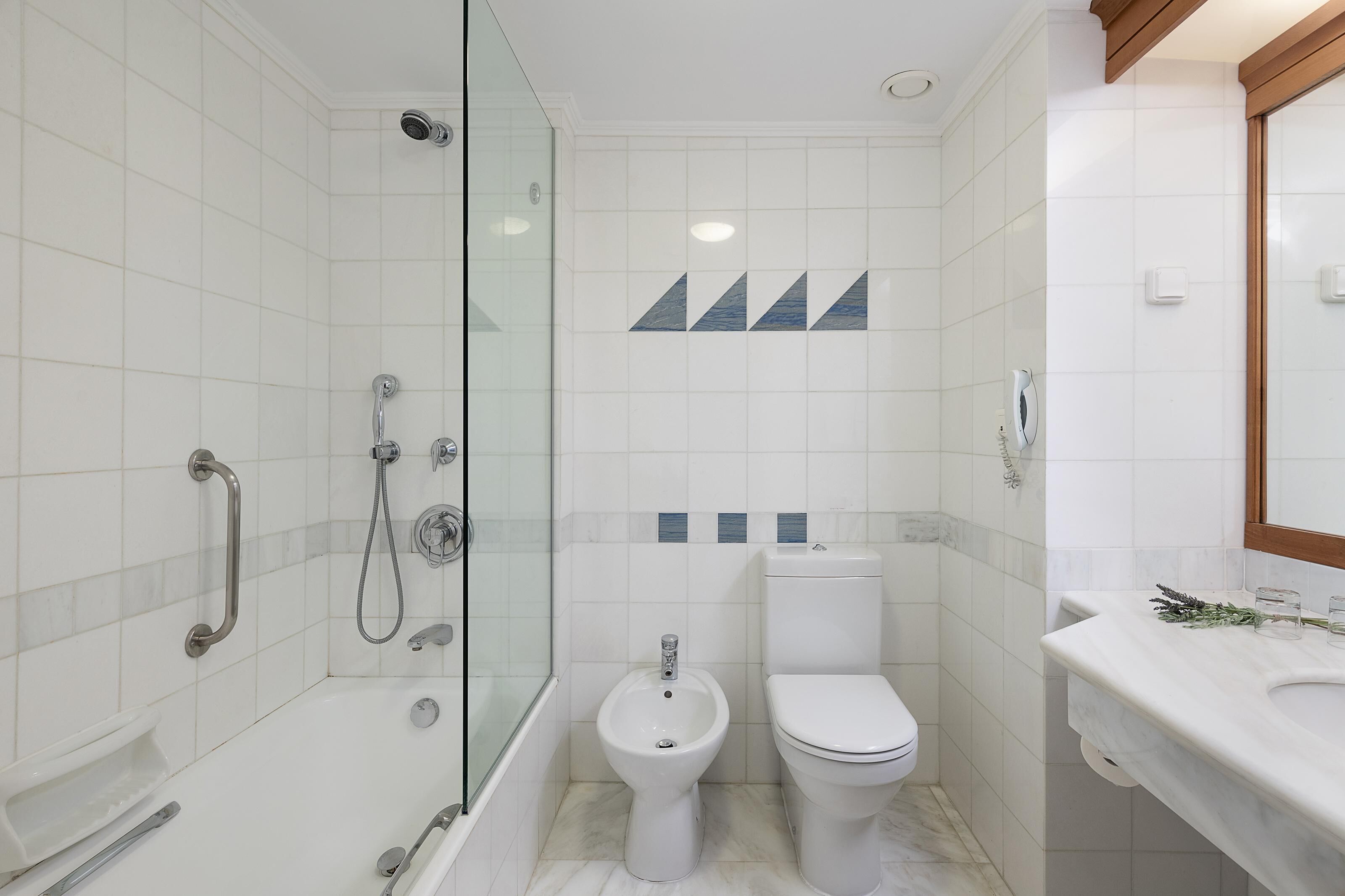 A modern bathroom with a glass-enclosed shower, a bidet, a toilet, and a marble countertop with a mirror.