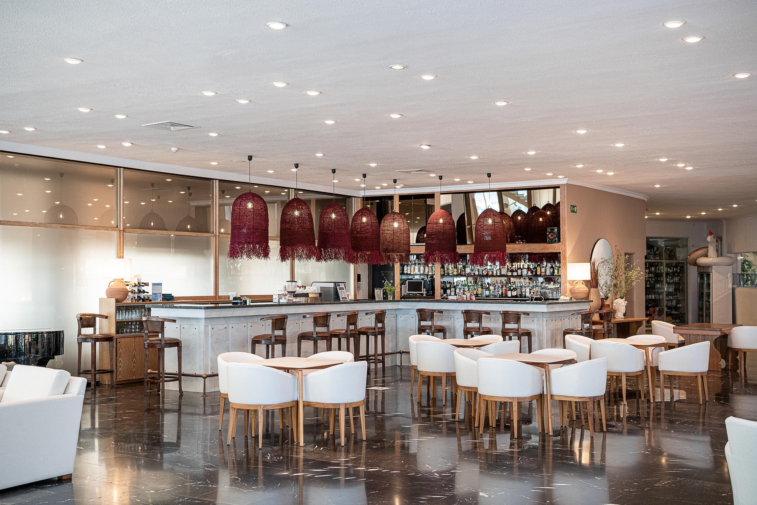 A modern bar area with a bar counter, white chairs, and a seating area with tables.