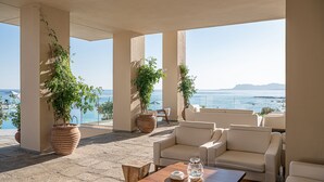 A sunlit outdoor seating area with a view of the sea, featuring potted plants and a wooden table. - Leptos Panorama Hotel (Chania)