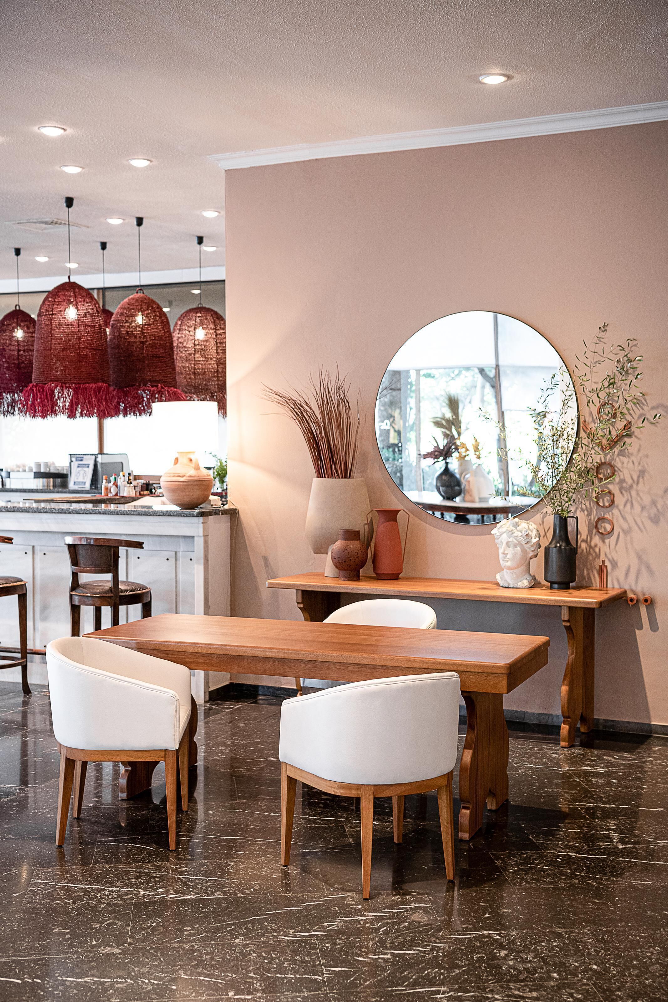 A modern dining area with a wooden table, white chairs, and a round mirror on the wall.