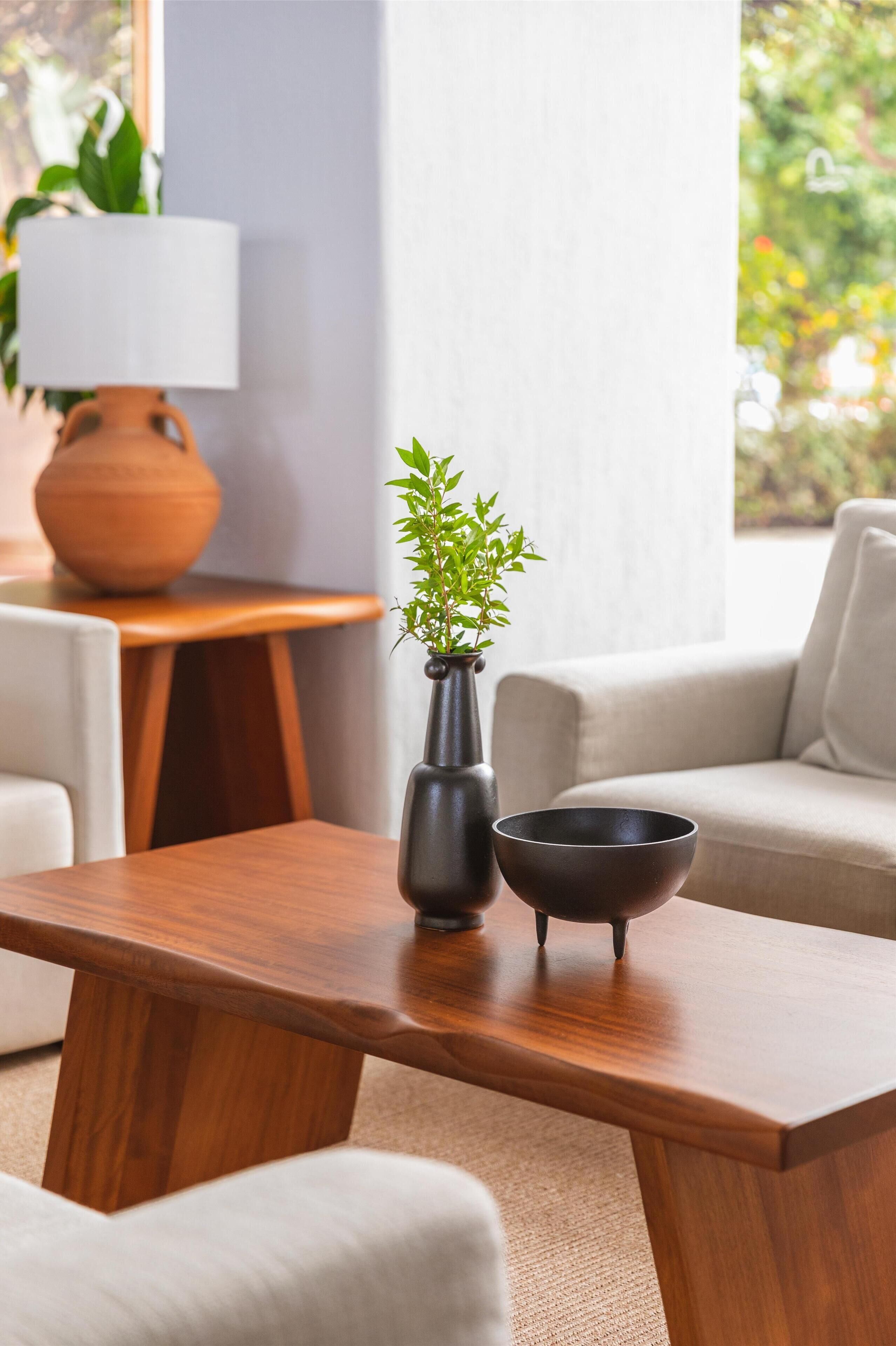 A wooden table with a vase and a bowl, a lamp, and a sofa in a modern living room.