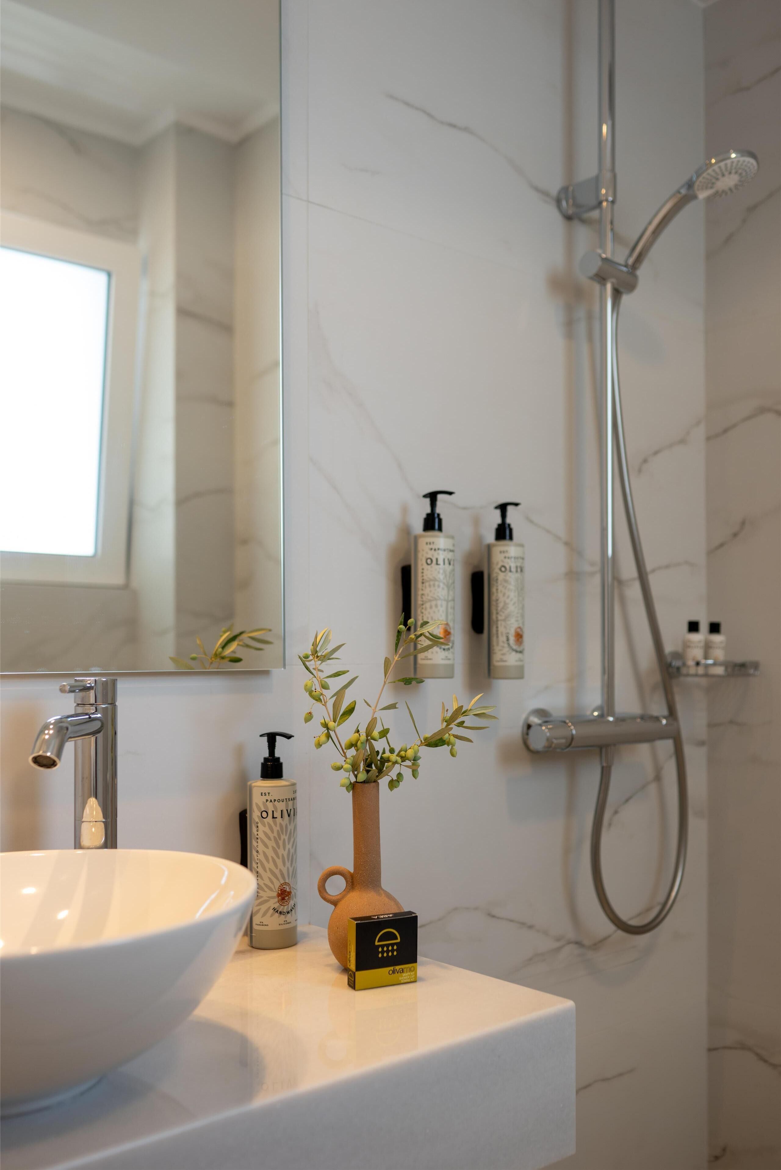A bathroom with a white sink, a mirror, a shower, and toiletries on the wall.