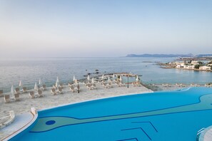 A pool with lounge chairs and umbrellas, overlooking a body of water and a coastal town.
