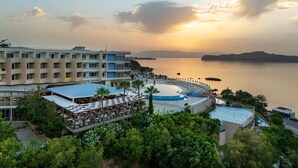 A resort with a pool, outdoor seating, and a view of the sea at sunset. - Leptos Panorama Hotel (Chania)