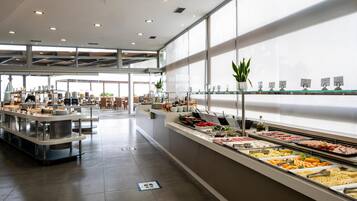 Zona de bufé con diversas opciones de comida, una zona de estar y grandes ventanales que dejan entrar luz natural.