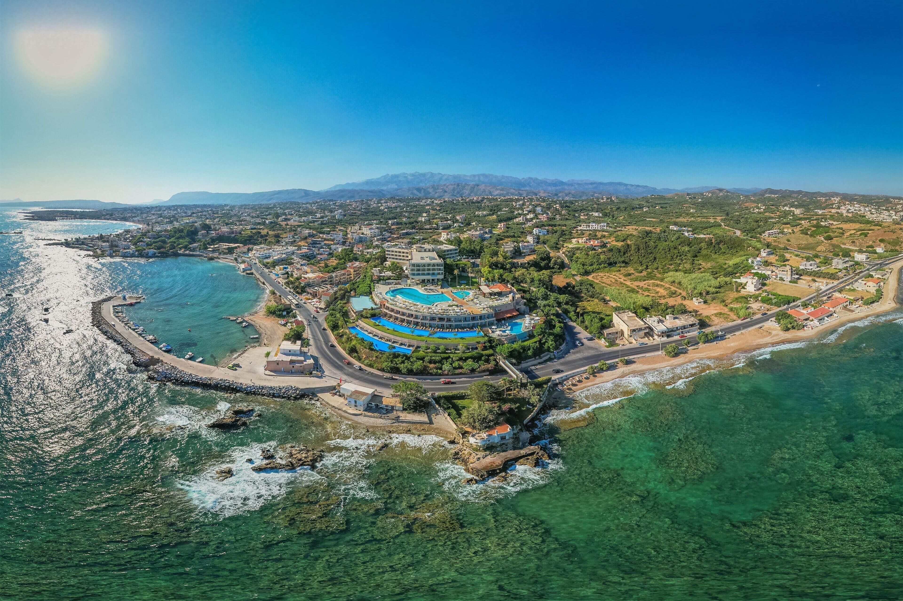 Vue aérienne d’une station balnéaire, avec un bâtiment central entouré d’une piscine, d’une plage et d’eaux bleues et cristallines.