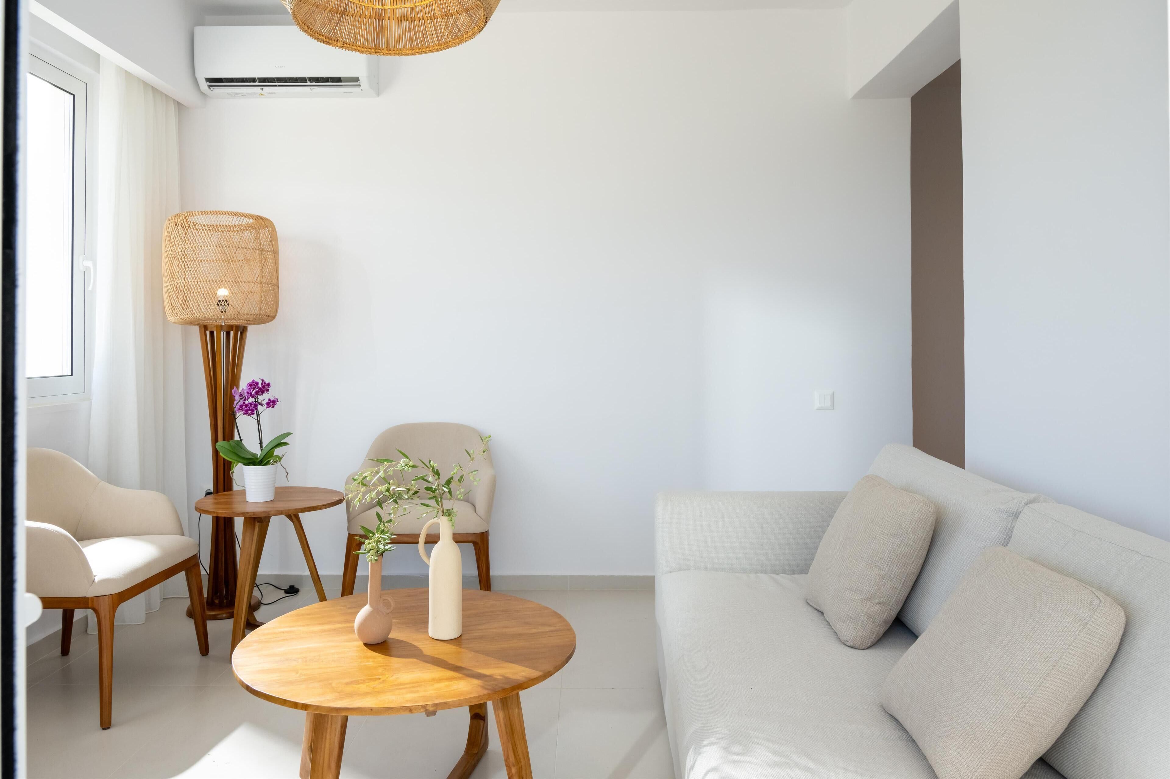 Una sala moderna con un sofá, una mesa redonda de madera y dos sillas. Hay una lámpara de pie grande de mimbre y una planta en maceta sobre una mesita.