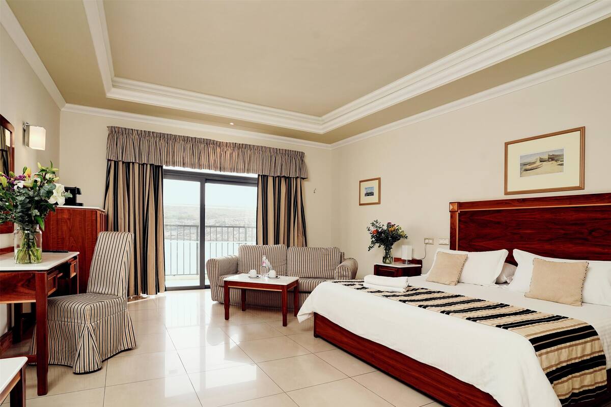 A hotel room with a large bed, a sofa, a chair, a small table, and a window with curtains.