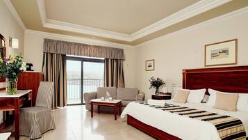 Habitación de hotel con una cama grande, un sofá, una silla, una mesita y una ventana con cortinas.