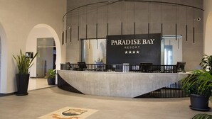 Een modern ontworpen receptiebalie bij Paradise Bay Resort, met een groot bord en potplanten.