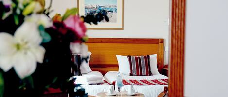 A hotel room with a wooden headboard, a bed with white and striped bedding, a framed picture on the wall, and a vase with flowers on the bedside table.