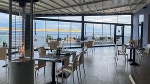 Een restaurant met grote ramen en uitzicht op de zee en een verre kustlijn.