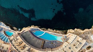 An aerial view of a resort with multiple swimming pools, sun loungers, and a rocky coastline. - Paradise Bay Resort (Mellieha)