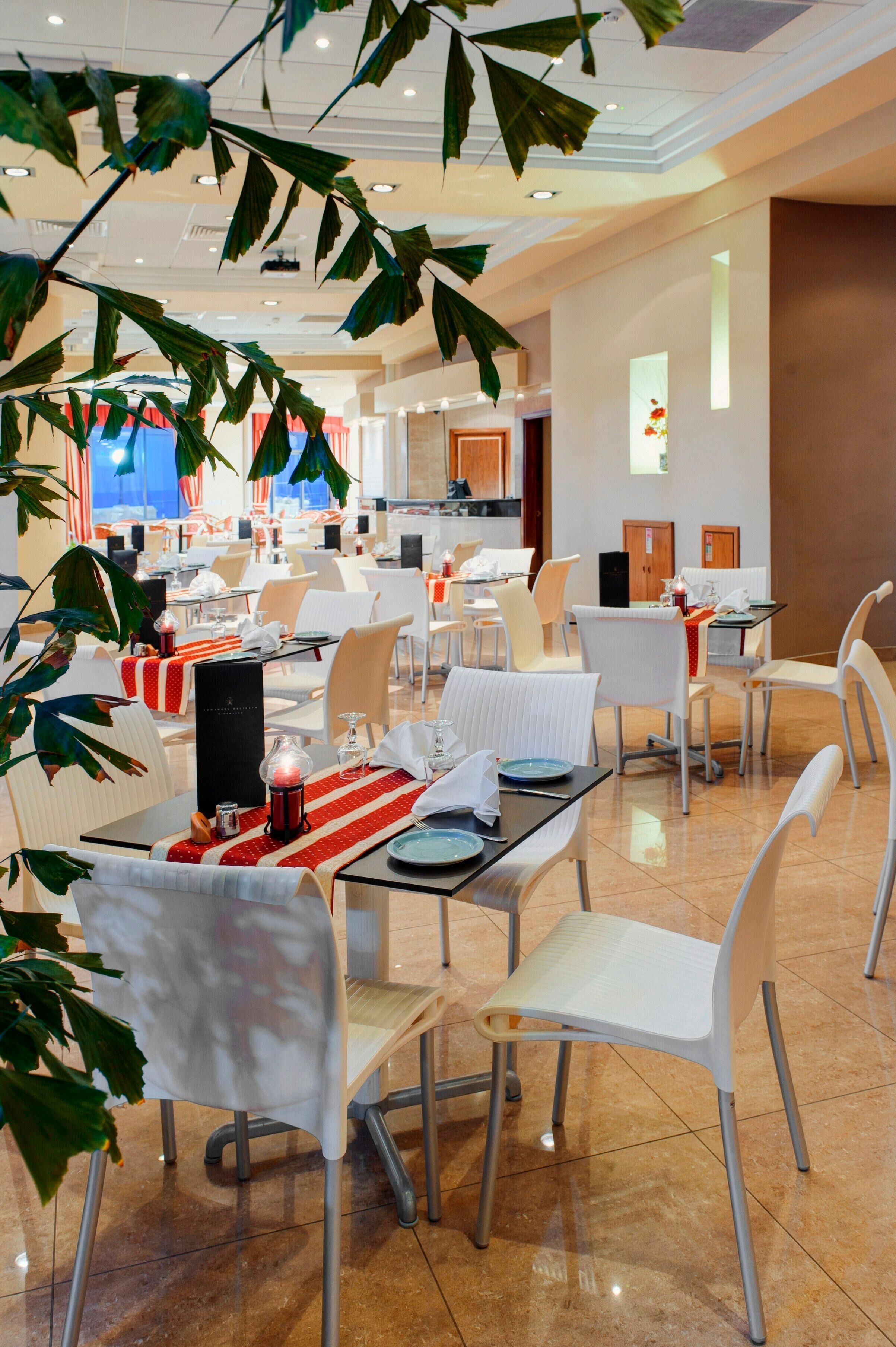 Zona pranzo con tavoli apparecchiati, sedie e un soffitto con illuminazione a incasso.