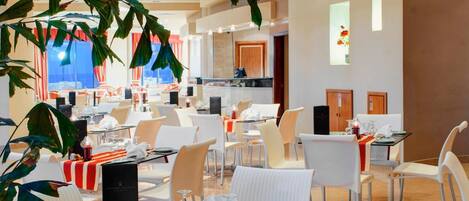 A dining area with tables set for service, chairs, and a ceiling with recessed lighting.