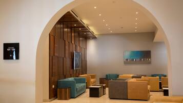 A modern lobby with a wooden wall panel, teal and mustard sofas, a flat-screen TV, and a painting.