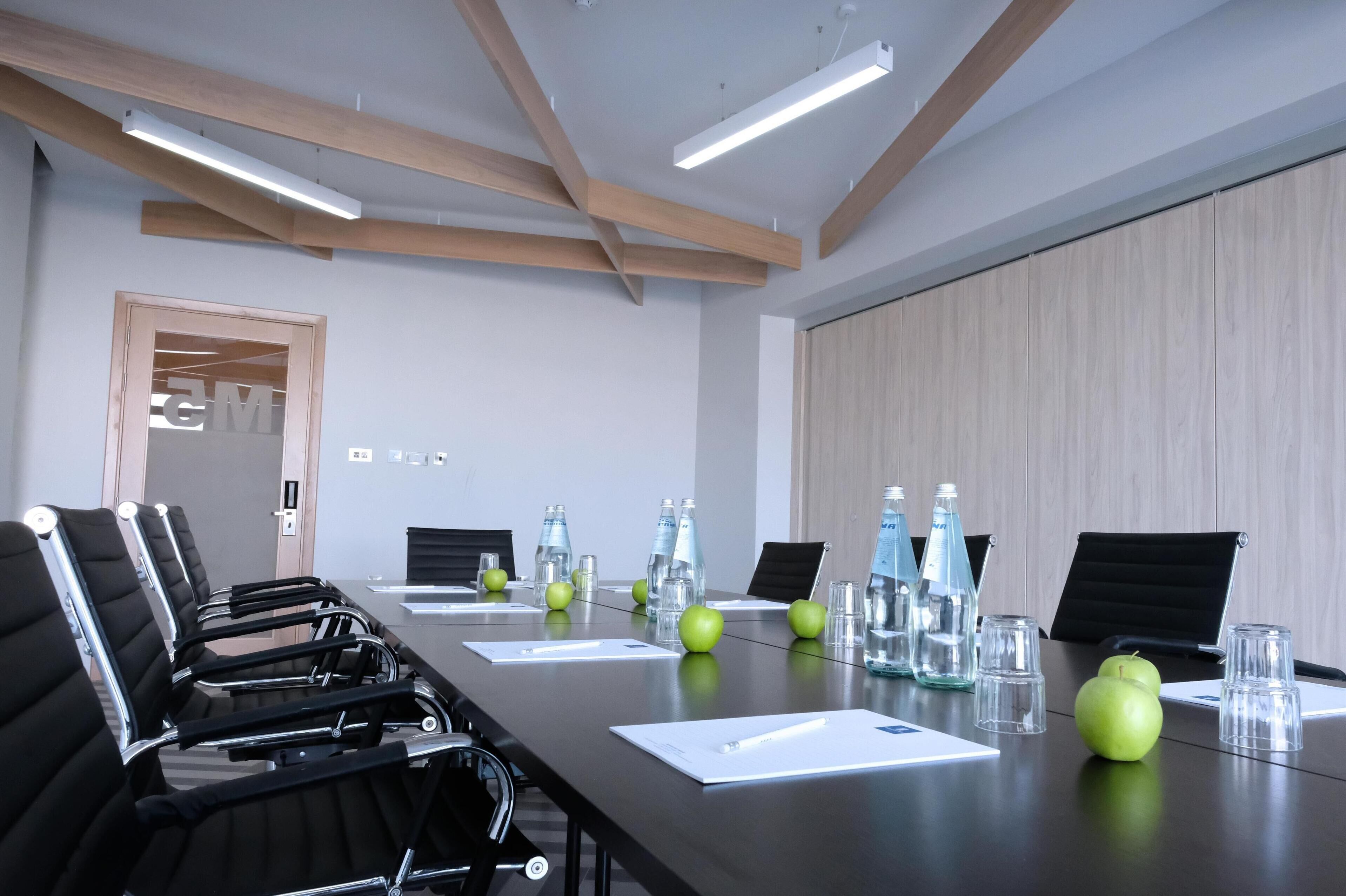 A conference room with a long table, black chairs, water bottles, and apples.