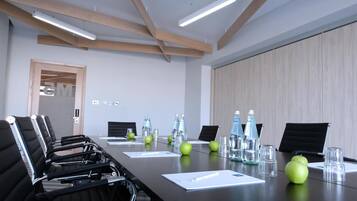 A conference room with a long table, black chairs, water bottles, and apples.