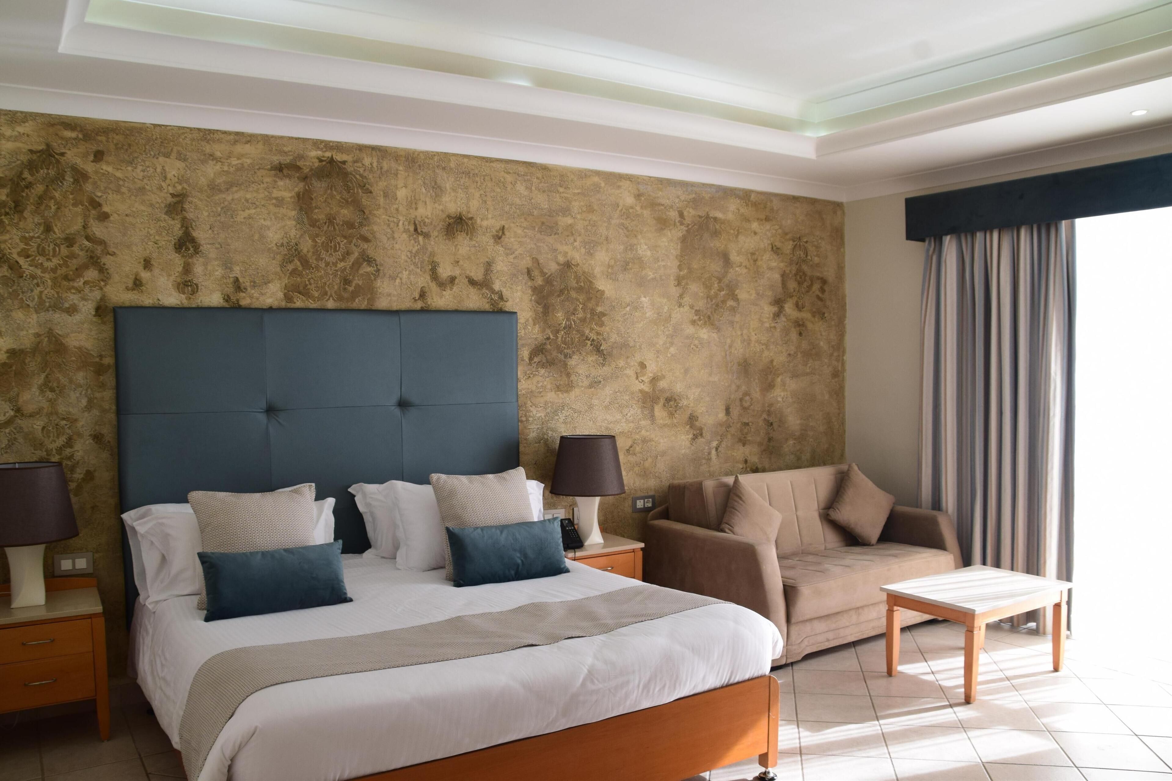 A hotel room with a large bed, a sofa, a small table, and a nightstand.