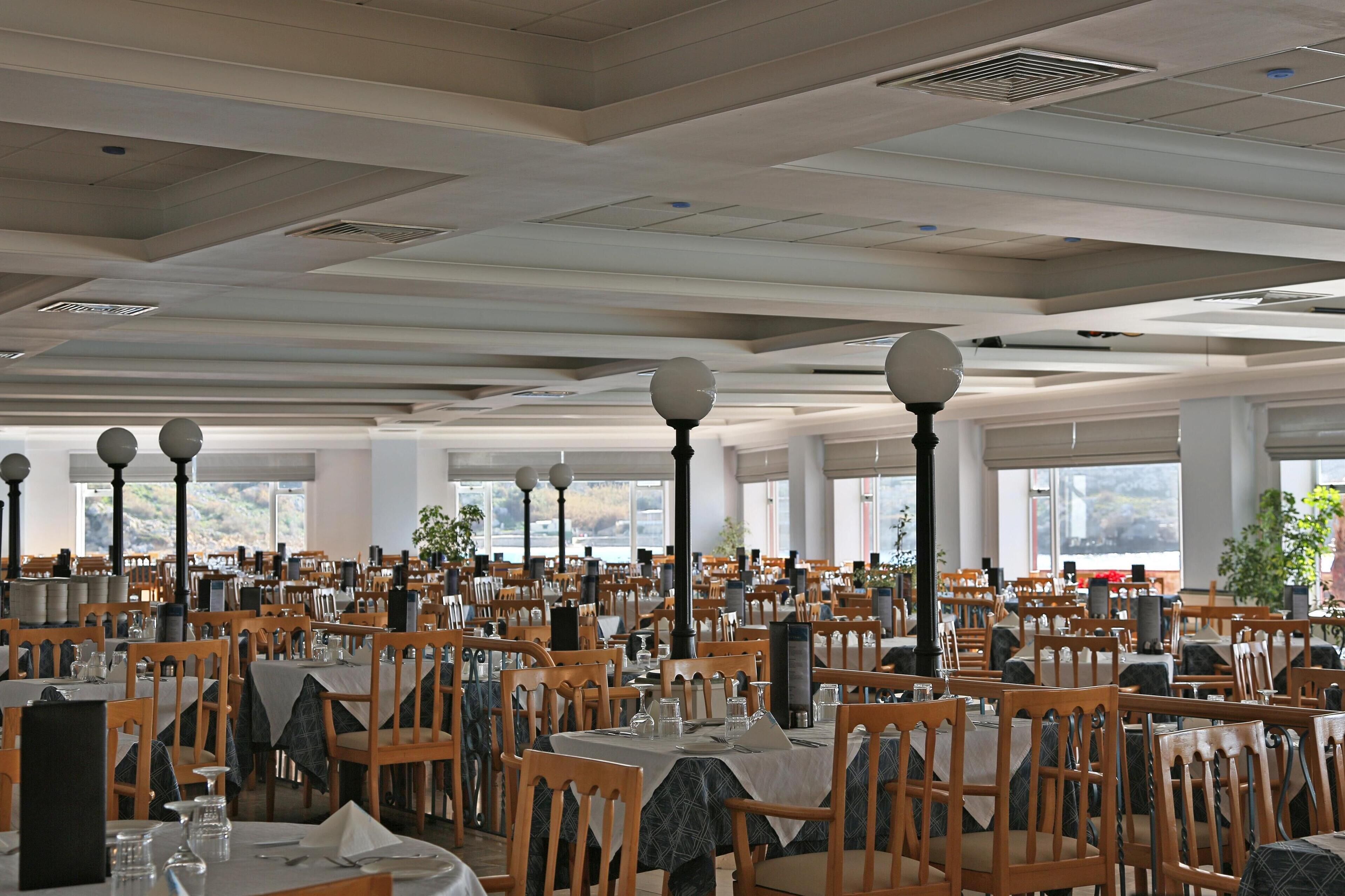 A spacious dining area with multiple tables and chairs, large windows, and decorative street lamps.