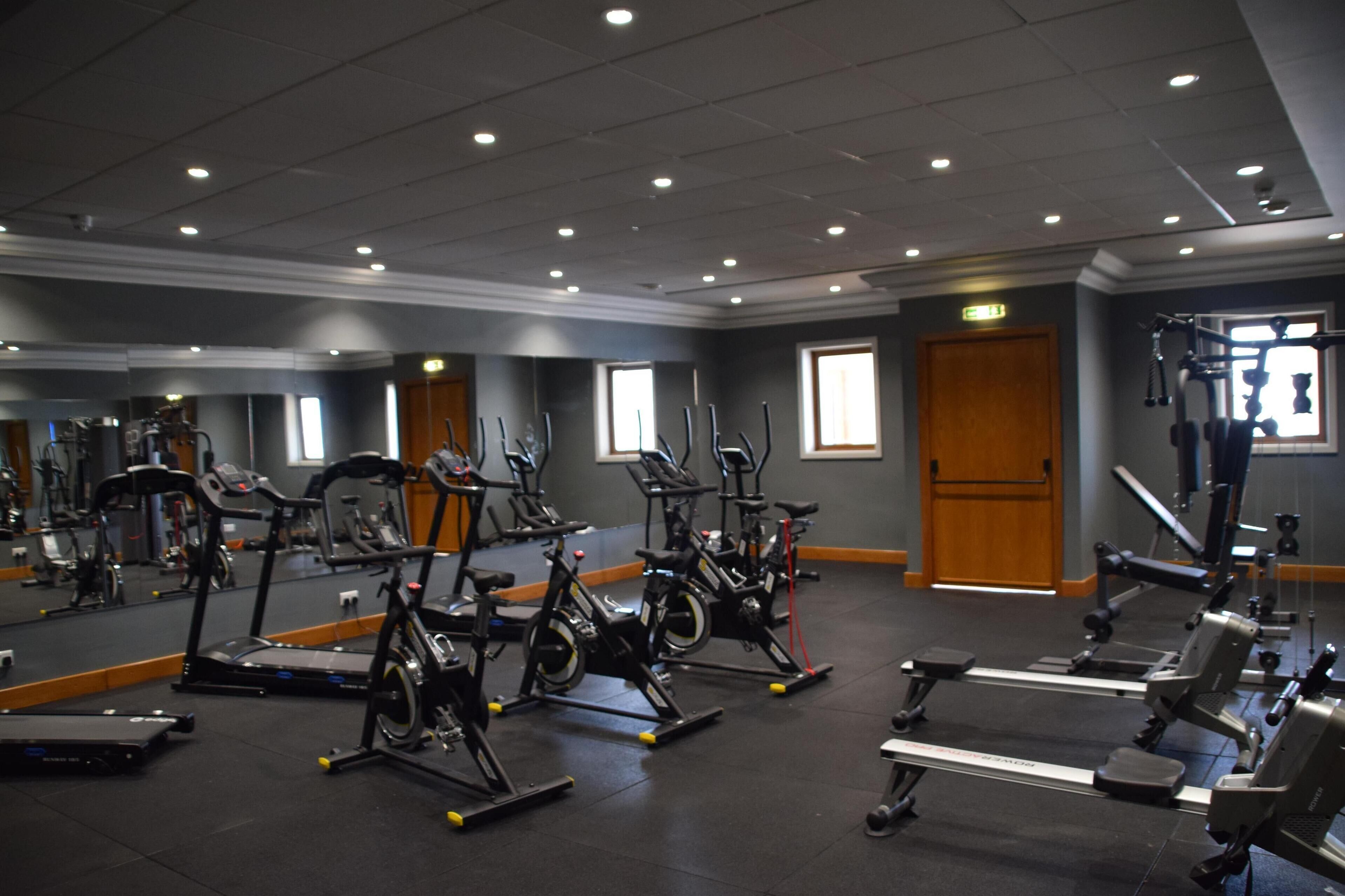 Une salle de sport équipée de divers appareils d’exercice, dotée d’un grand miroir et d’une porte donnant sur une autre pièce.