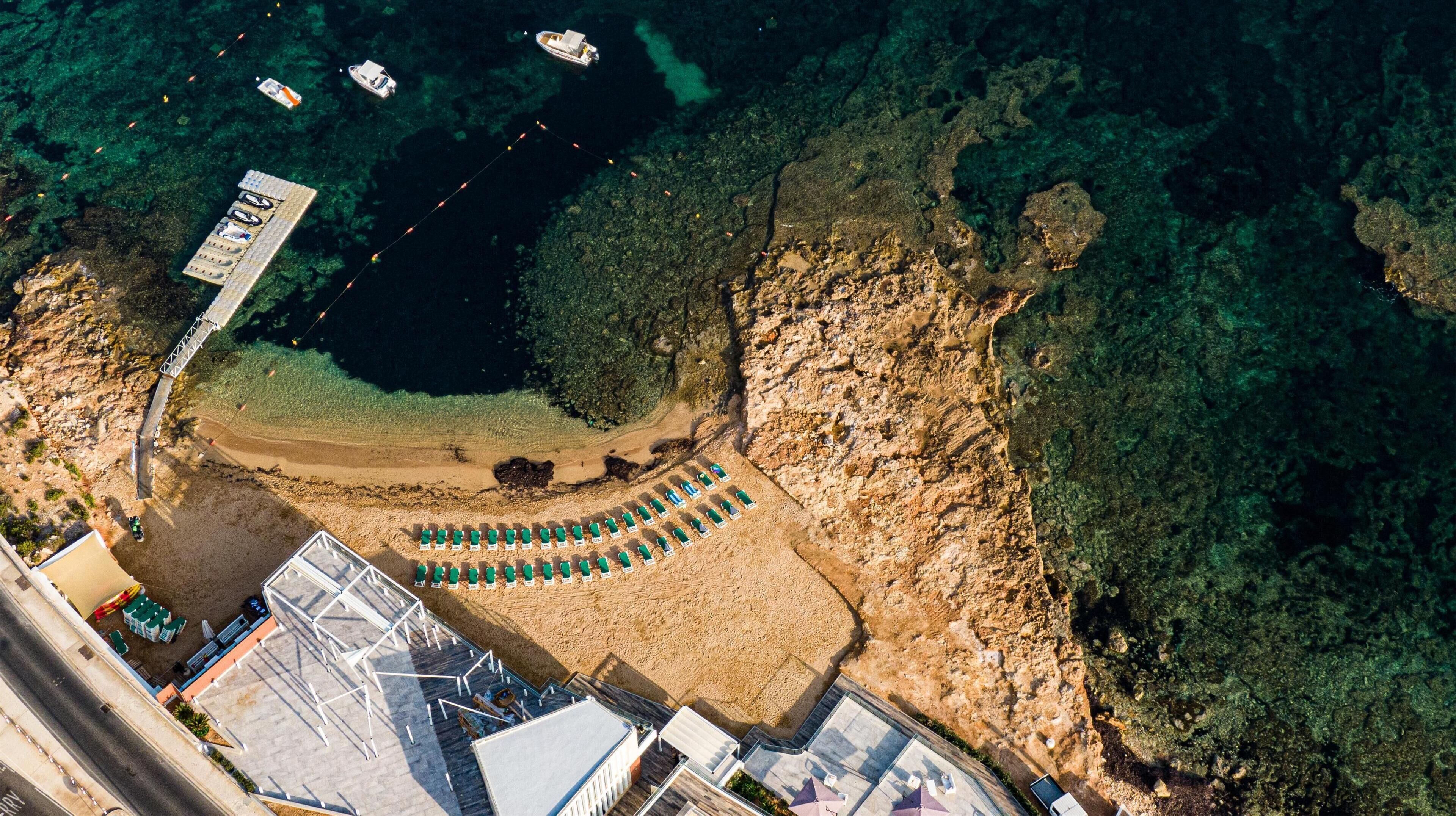 Vista aérea de una zona costera con una playa arenosa, un muelle y barcos en el agua.