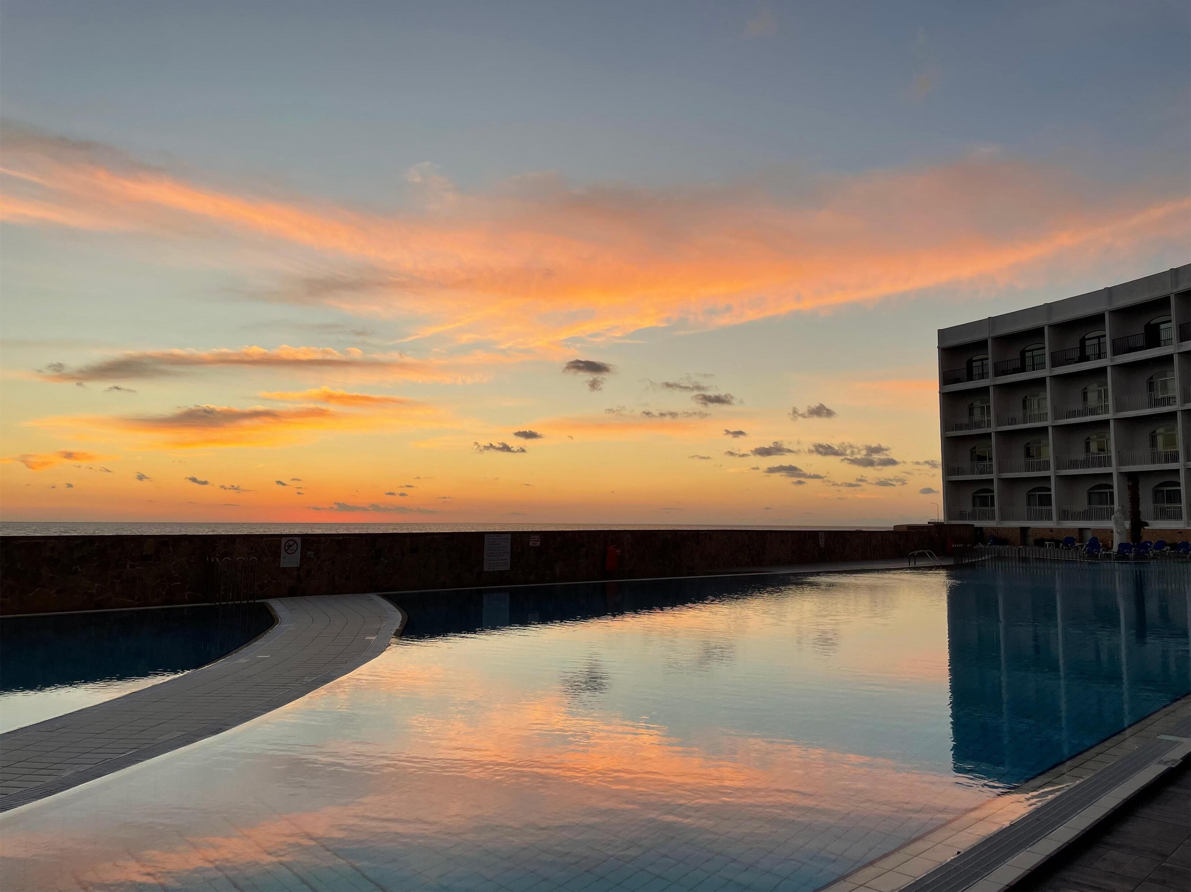 A swimming pool with a sunset view, a building with balconies, and a stone wall.