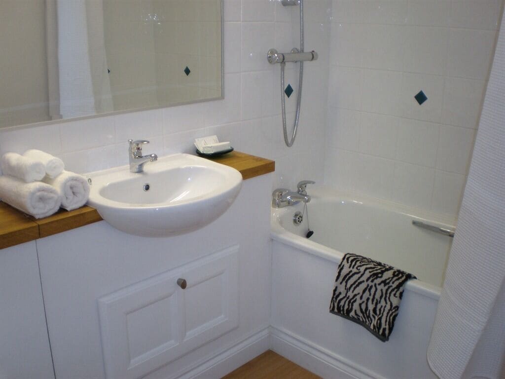 A bathroom with a white sink, a bathtub, and a shower. There are towels on the sink and a towel hanging on the bathtub.
