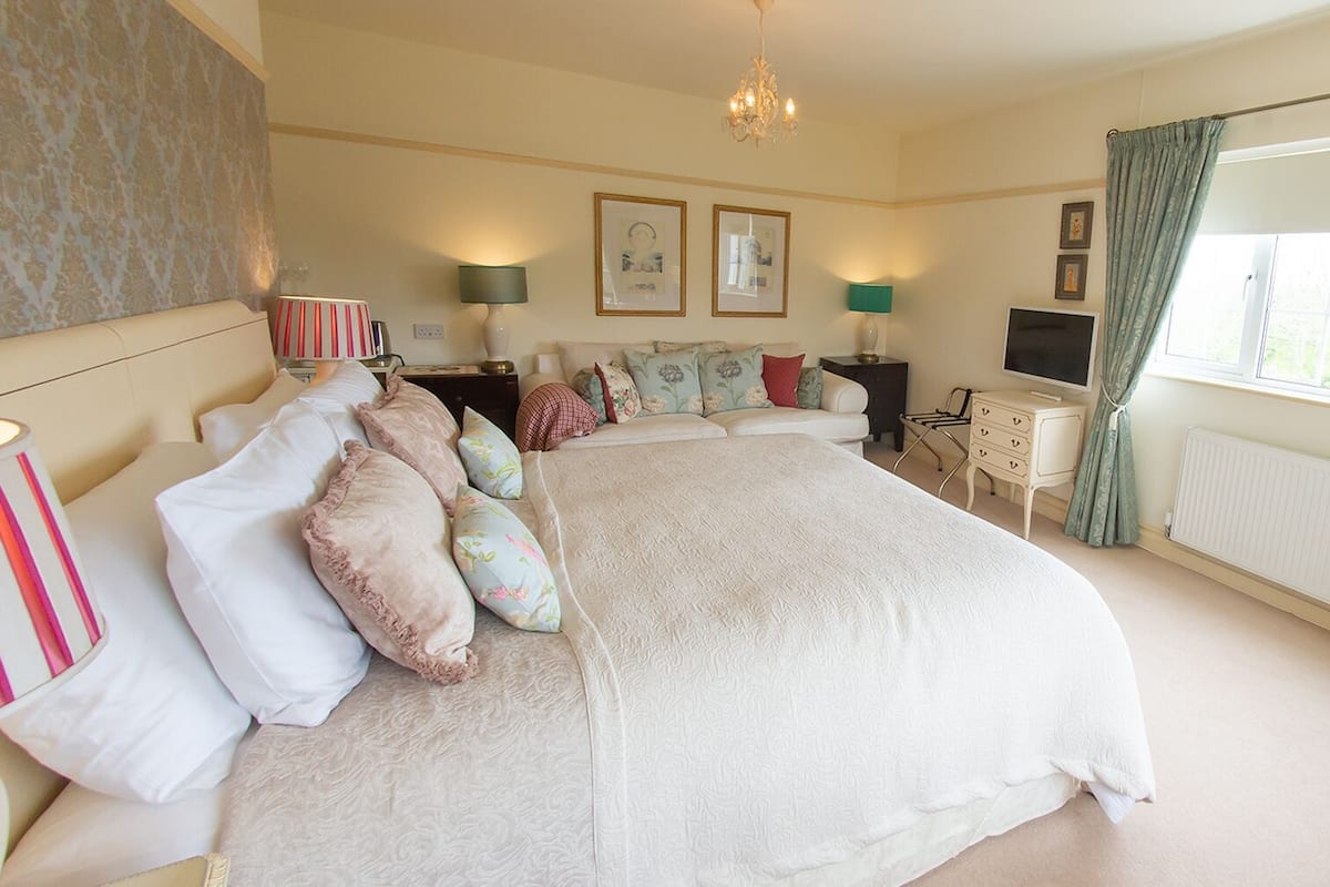 A spacious bedroom with a large bed, bedside lamps, a dresser, a television, and framed pictures on the wall.