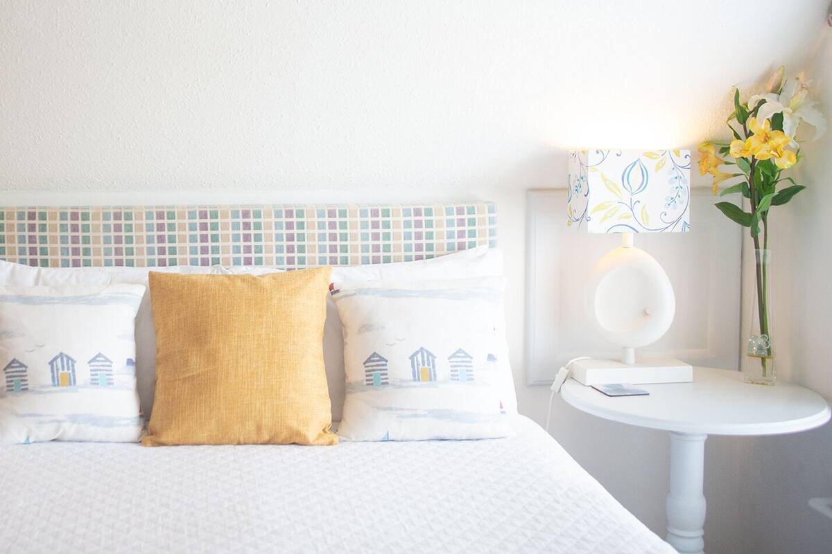 A neatly made bed with a patterned headboard, two bedside tables with lamps, and a vase with flowers on a small table.