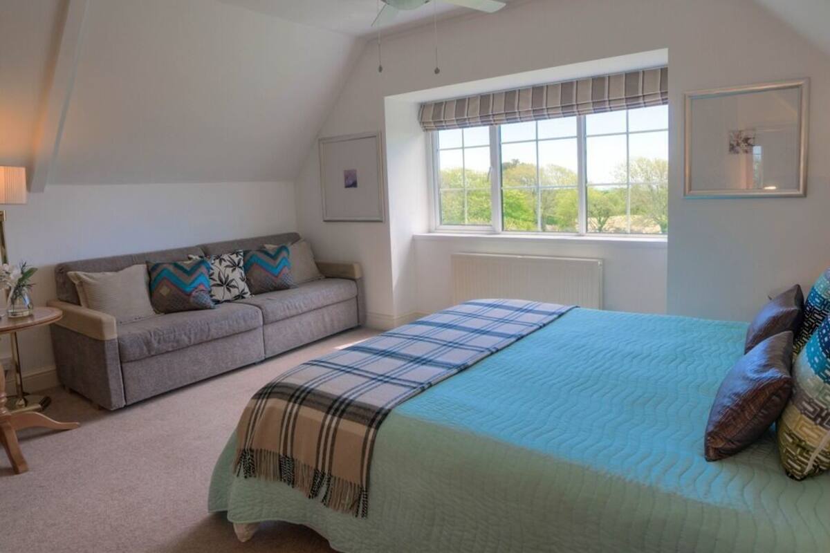 A bedroom with a bed, a window with curtains, a ceiling fan, and a sofa.