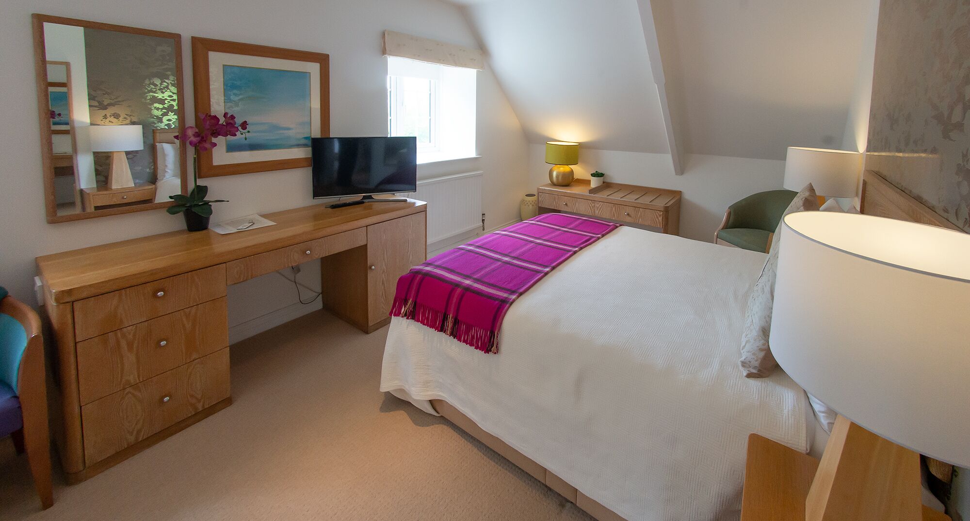 Une chambre à coucher avec un lit, un bureau, une télévision, une lampe et une fenêtre.