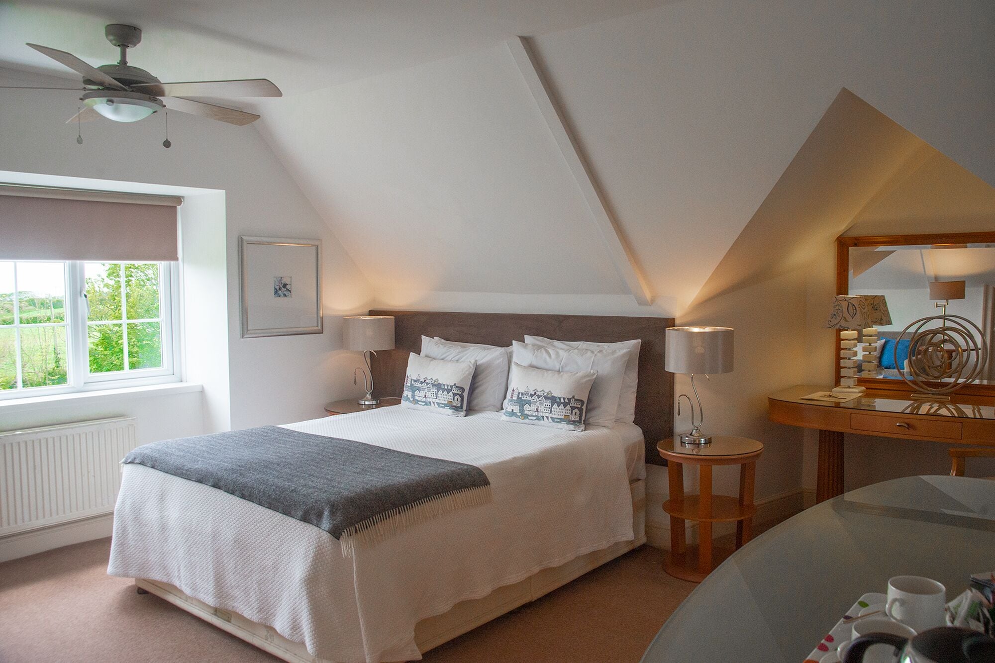 A bedroom with a bed, bedside tables, a desk, a mirror, and a ceiling fan.