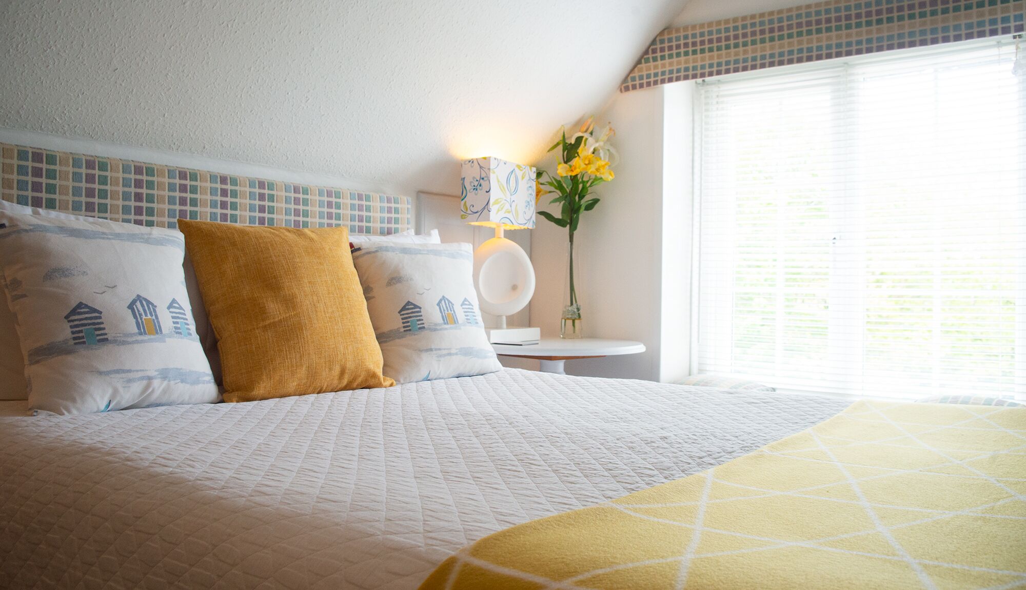 A neatly made bed with a quilted white bedspread and two pillows, one with a nautical design and another in mustard yellow.