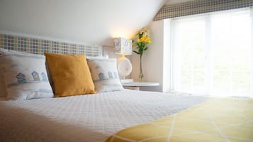 Una cama bien tendida con una colcha blanca acolchada y dos almohadas, una con diseño náutico y otra de color mostaza.
