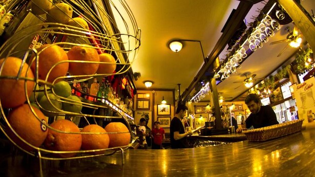 Zona comercial con un expositor de frutas metálico, un área de bar y un espacio de estar con una fuente.