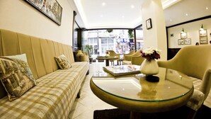 Un hall de hotel con un sofá, sillones, una mesa redonda y un jarrón de flores.