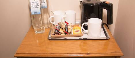 A tray with two white mugs, two bottles of water, a coffee maker, and a tray of snacks on a wooden table.