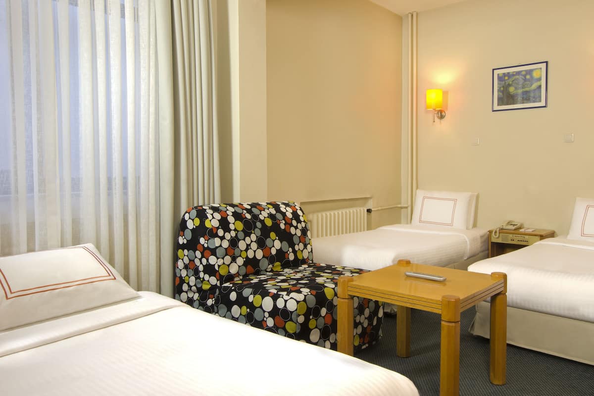 Hotellihuone, jossa on kaksi sänkyä, pilkkukuviollisella päällisellä varustettu tuoli, pieni puinen pöytä ja kaksi seinälle asennettua lamppua.