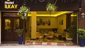 Entrada de hotel con interior amarillo, un mostrador de recepción y una zona de estar con sillas y una mesa.